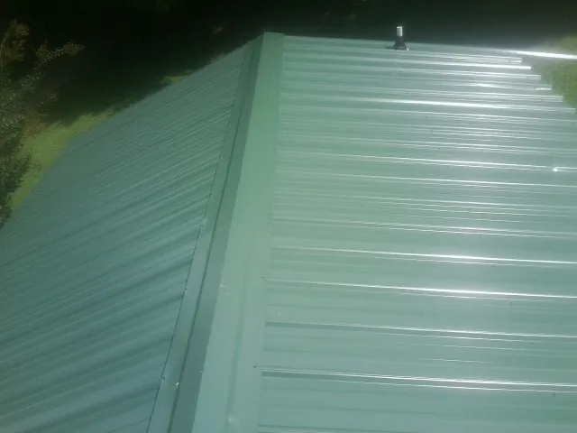 New green metal panels meeting at the ridge of a roof — Flat Roof Repair work by our crew in Pennsauken