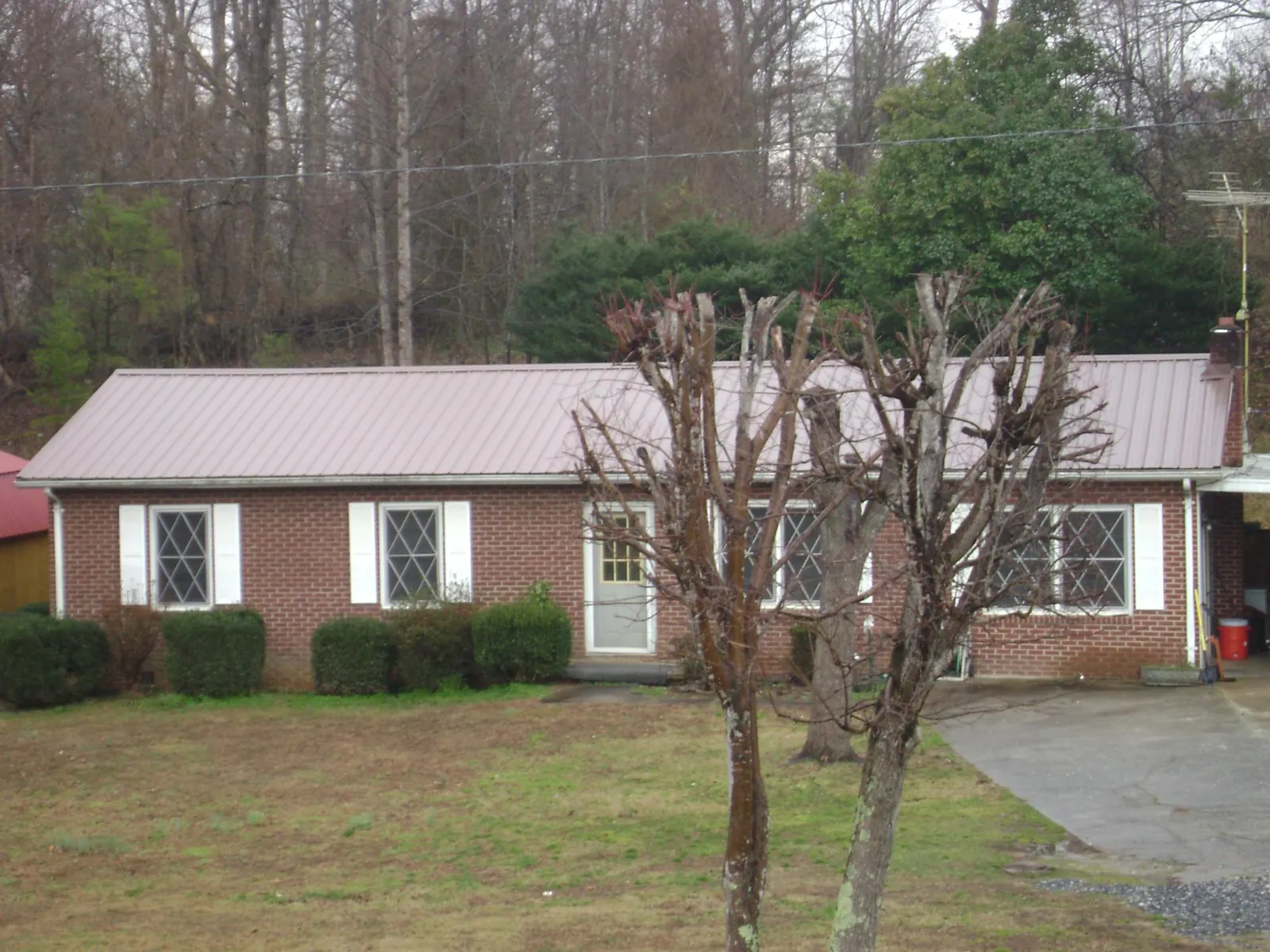 Mauve metal roof on a brick ranch home behind bare trees in Pennsauken