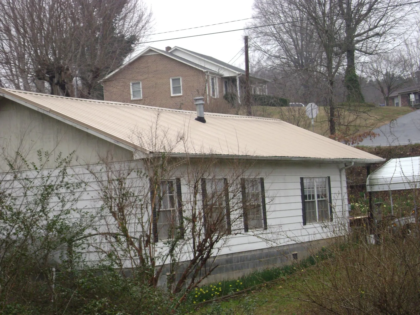 Tan metal roof on a white sided house set into a hillside — Commercial Roofing by Roofing Brothers in Pennsauken